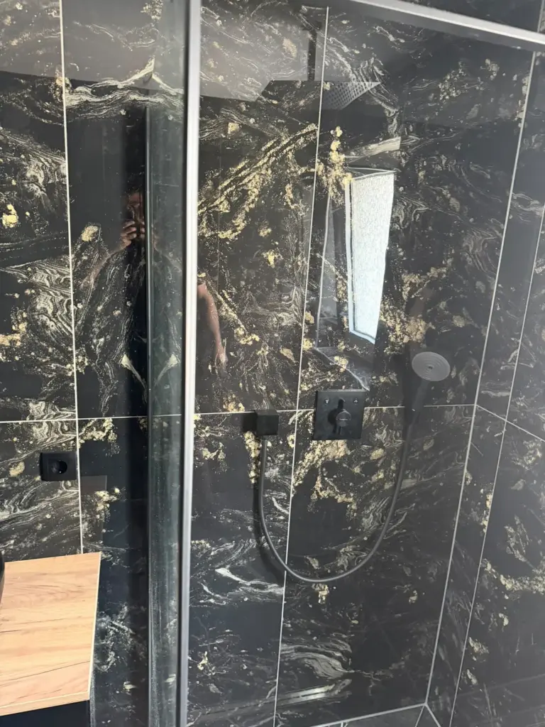 Dusche mit Glasabtrennung und dunklen Fliesen in Marmoroptik